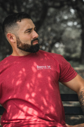 Man wearing a red t-shirt with text, sitting outdoors with trees in the background
