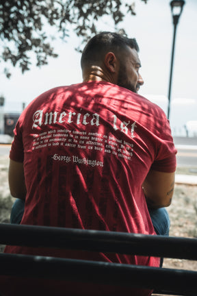 Man wearing a red t-shirt with text on the back, sitting outdoors.