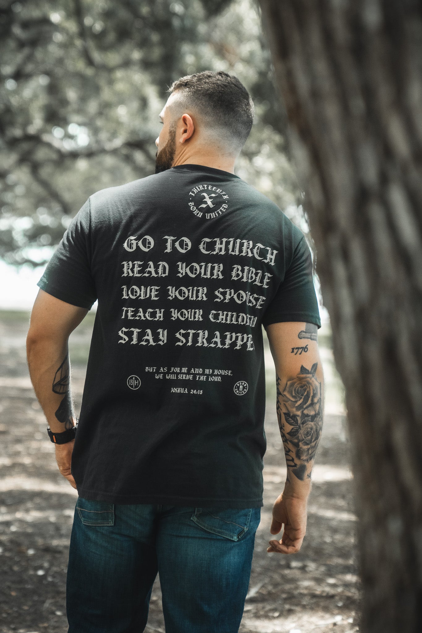 A tattooed man stands outdoors, seen from behind, wearing the Kingdom Protector Premium Tee by Born United Private Label—perfect for fans of Bible verse wall art and those seeking faith-inspired motivation.