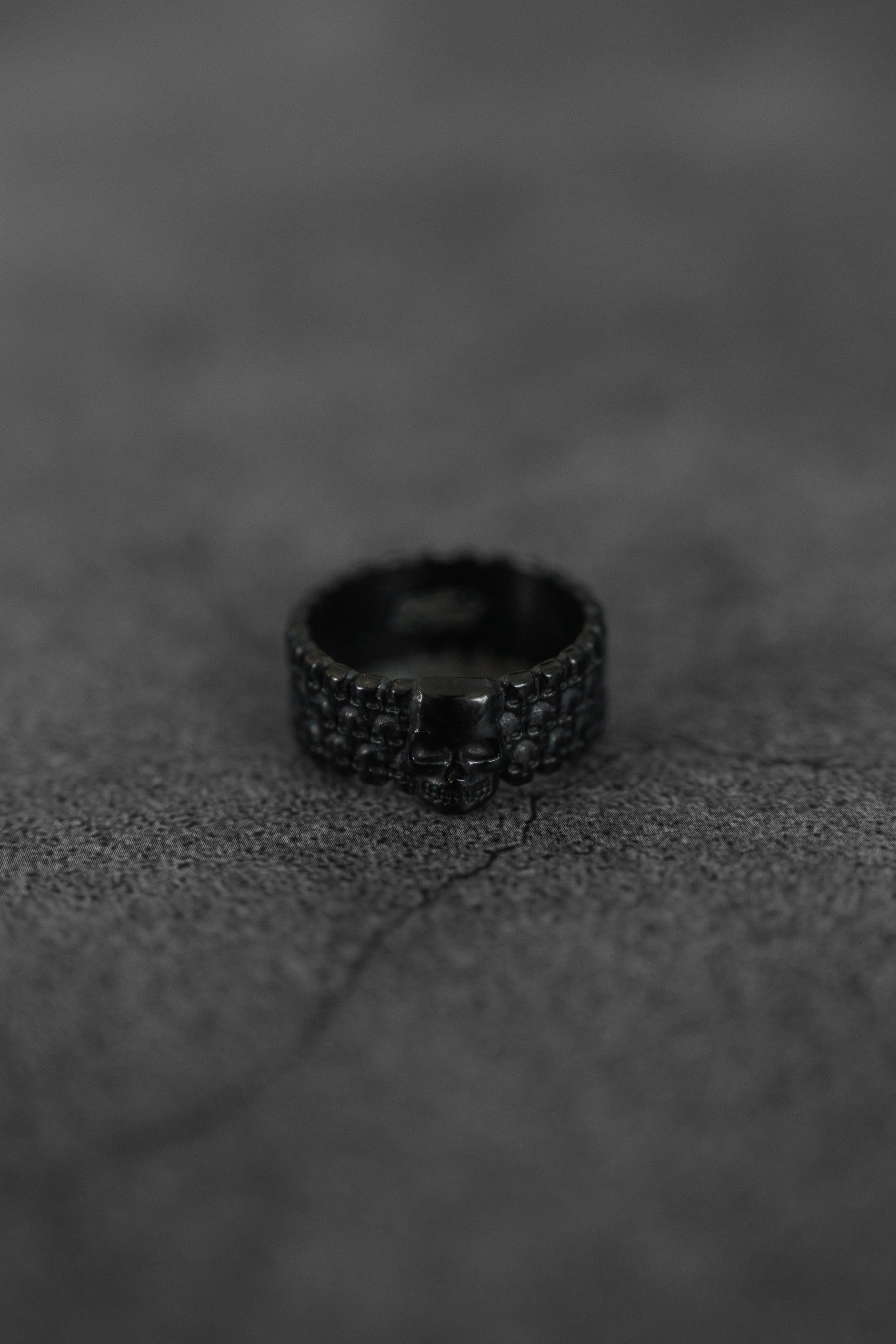 The Relentless Betrayal Kill Switch Blackout Ring, featuring a bold skull design and matte black finish, rests on a cracked, textured dark grey surface.