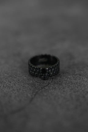The Relentless Betrayal Kill Switch Blackout Ring, featuring a bold skull design and matte black finish, rests on a cracked, textured dark grey surface.