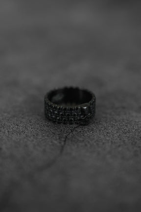 The Kill Switch Blackout Ring by Relentless Betrayal, featuring a small skull detail and matte black finish, sits on a rugged dark surface, evoking a bold and dramatic vibe.