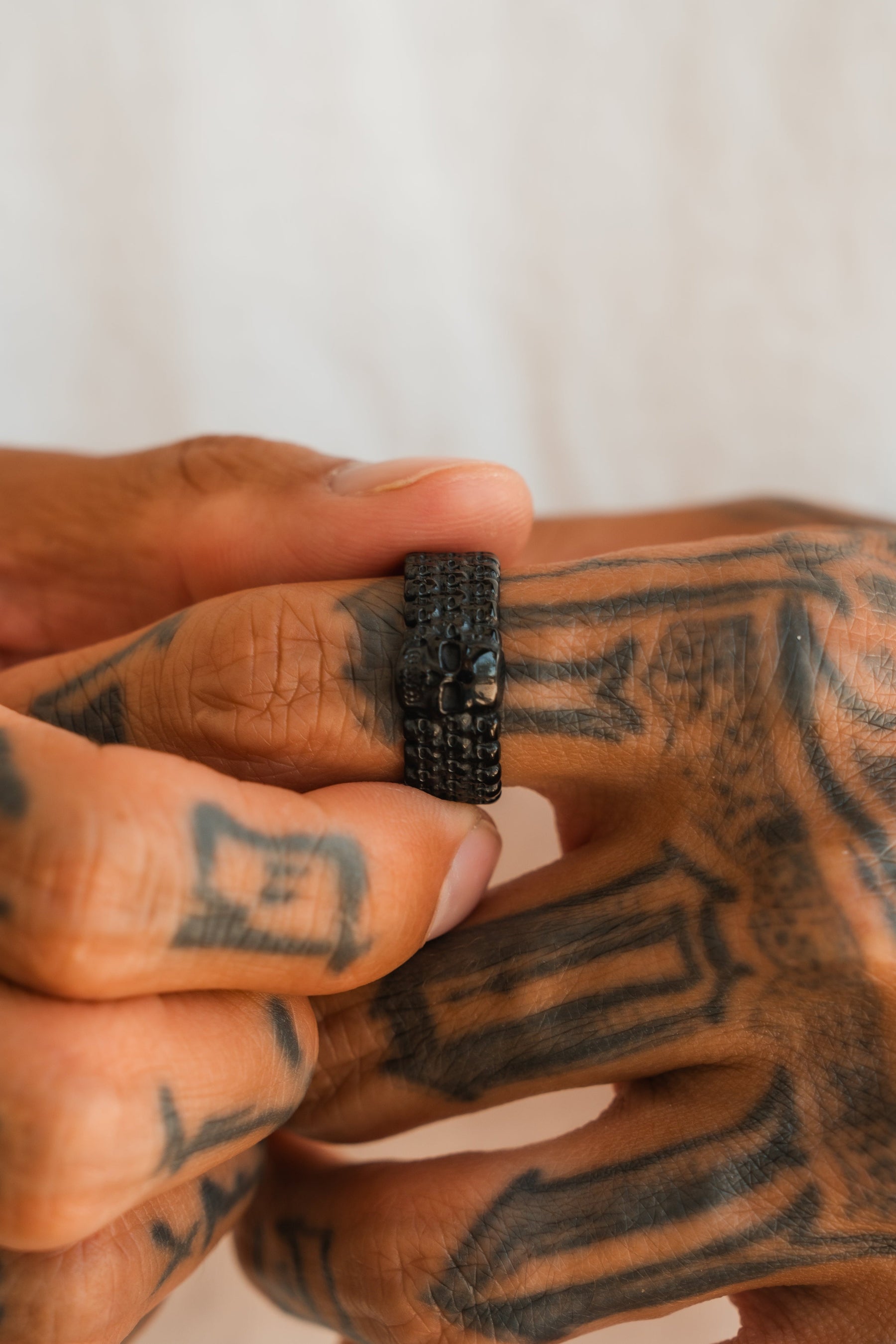 A close-up of tattooed hands holding a Relentless Betrayal Kill Switch Blackout Ring, with intricate finger and hand tattoos visible against a neutral background.