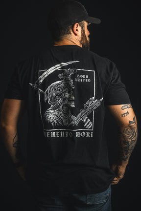 A man facing away wears a black cap and a black T-shirt from Born United Private Label’s “Memento Mori” collection, featuring a striking graphic of a skeleton warrior and the text “Memento Mori” and “Born United” on the back.