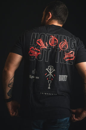 A man stands with his back to the camera, wearing the 13th brand’s Nothing But the Blood Premium Tee, a black shirt featuring bold red and white graphic text and symbols.