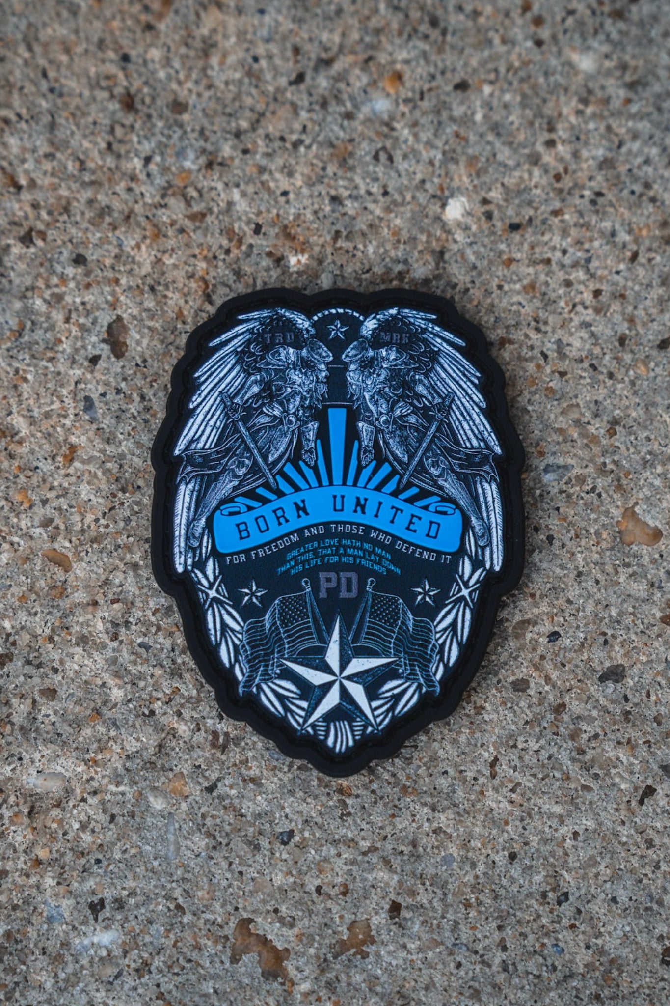 A black and blue embroidered patch featuring a detailed eagle design with the text 'BORN UNITED' and 'Tucson, Arizona', placed on a textured concrete surface.