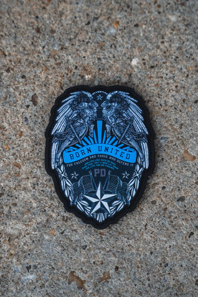 A black and blue embroidered patch featuring a detailed eagle design with the text 'BORN UNITED' and 'Tucson, Arizona', placed on a textured concrete surface.