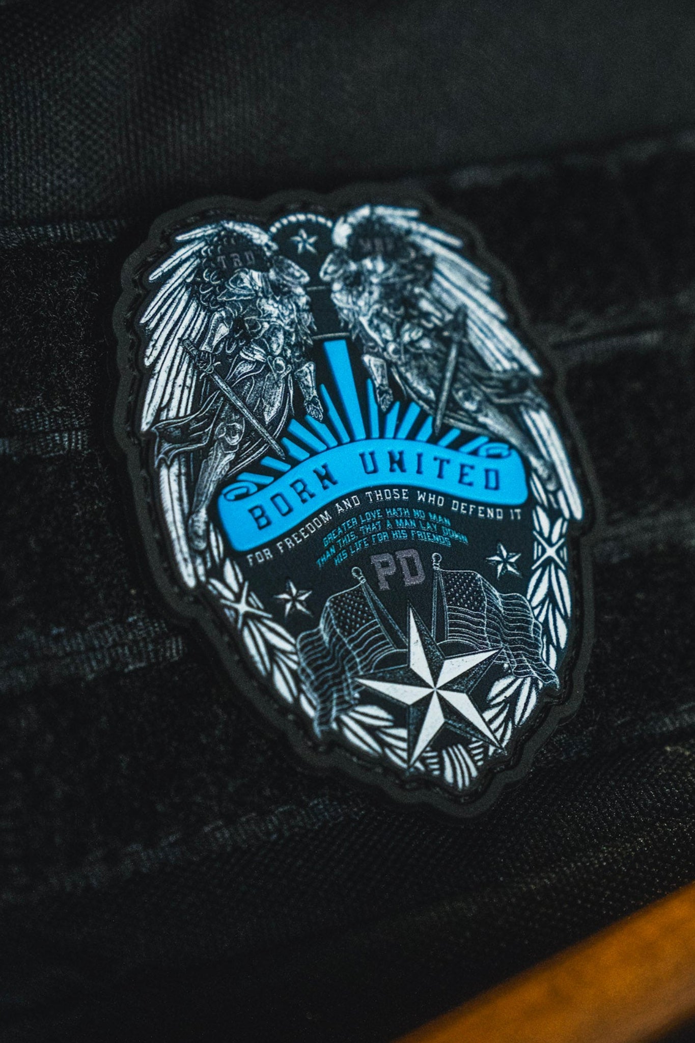 A close-up of a black fabric patch featuring a stylized eagle and the text 'BORN UNITED' with additional text below, attached to a black textured bag.