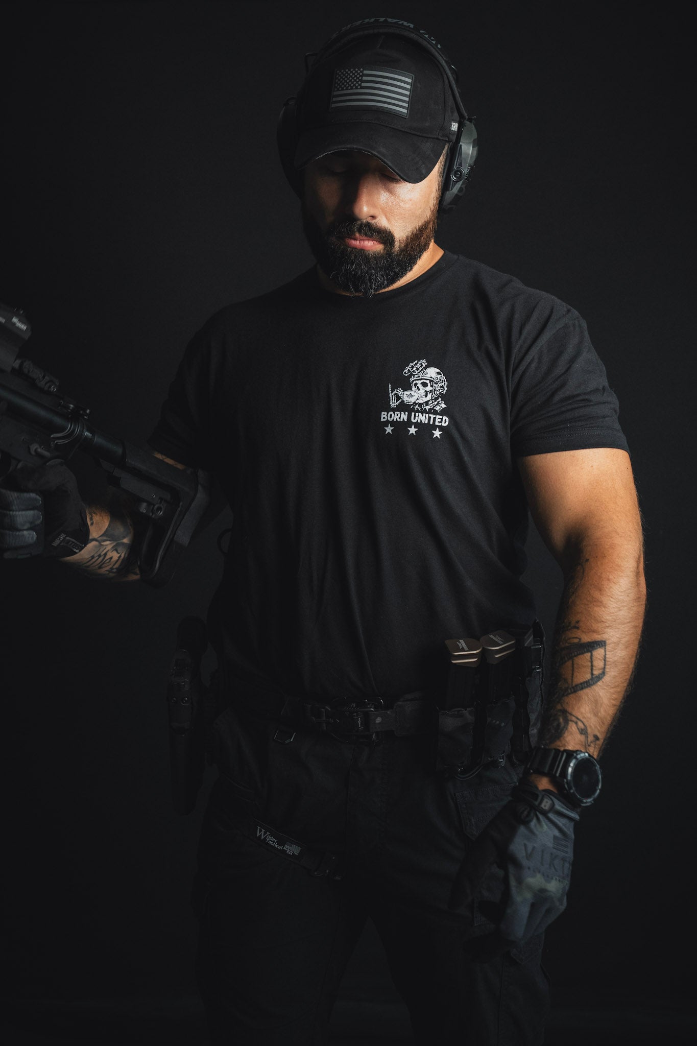 A man dressed in black tactical gear and cap, sporting gloves and headphones while holding a firearm against a dark backdrop—proving that with the Born United Private Label’s “Tea Party,” he’s definitely ready for action, not just sitting down for afternoon tea.