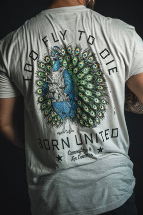 Wearing the “Too Fly To Die” T-shirt from the Born United Private Label, a person sports a bold design of a peacock holding a rifle with striking text: Too fly to die, born united, camouflage is for cowards.