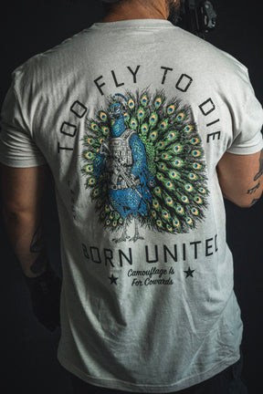 A person wearing the Born United Private Label “Too Fly To Die” T-shirt, which showcases a peacock in tactical gear and features the phrases “TOO FLY TO DIE,” “BORN UNITED,” and “Camouflage is for Cowards.”.