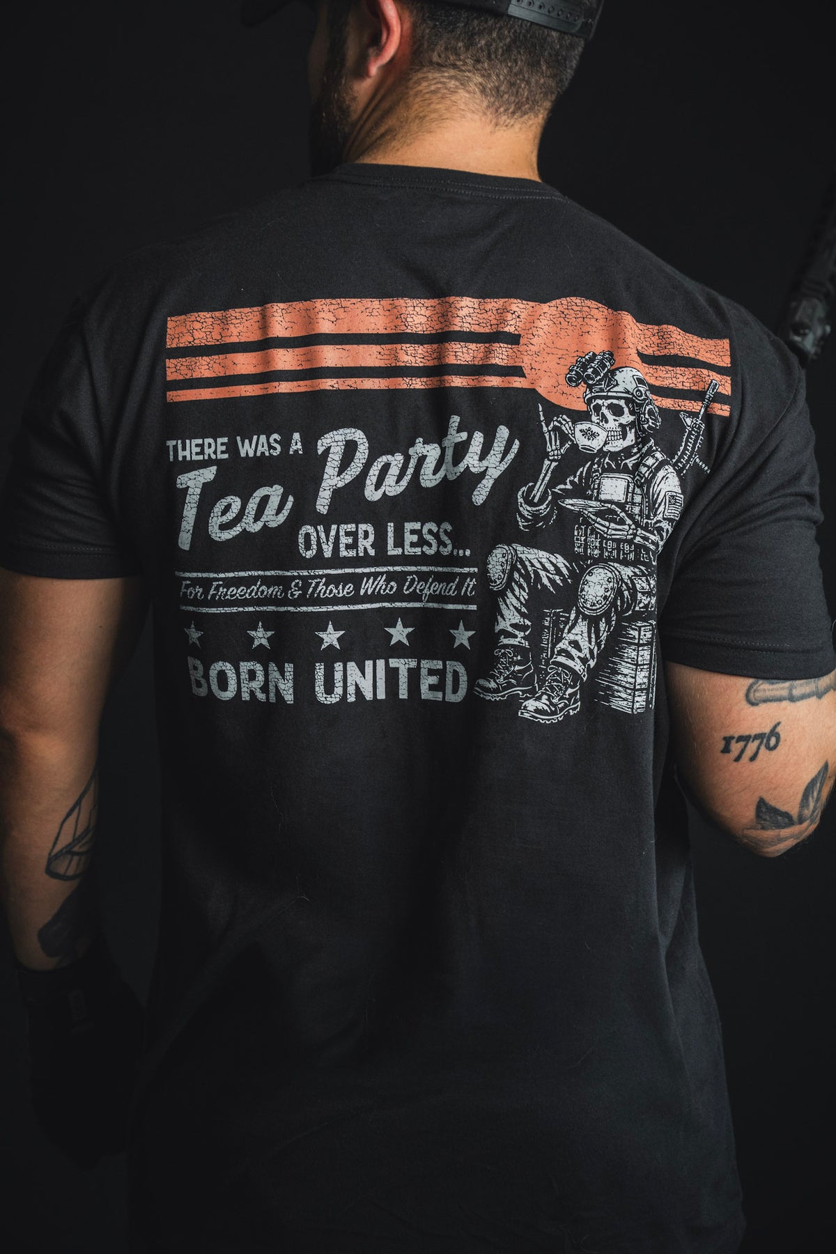 A person wearing the Born United Private Label “Tea Party” black T-shirt featuring a graphic of a skeleton holding a rifle and themed text.