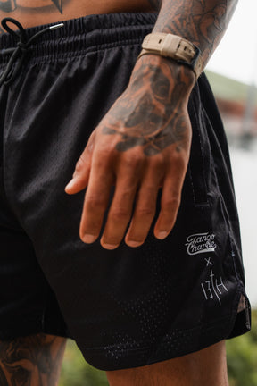 A close-up of a tattooed person wearing Tango Charlie Apparel Men's Mesh Lifestyle Shorts | 5.5" - Lift Heavy Pray Hard Black, paired with a beige watch.
