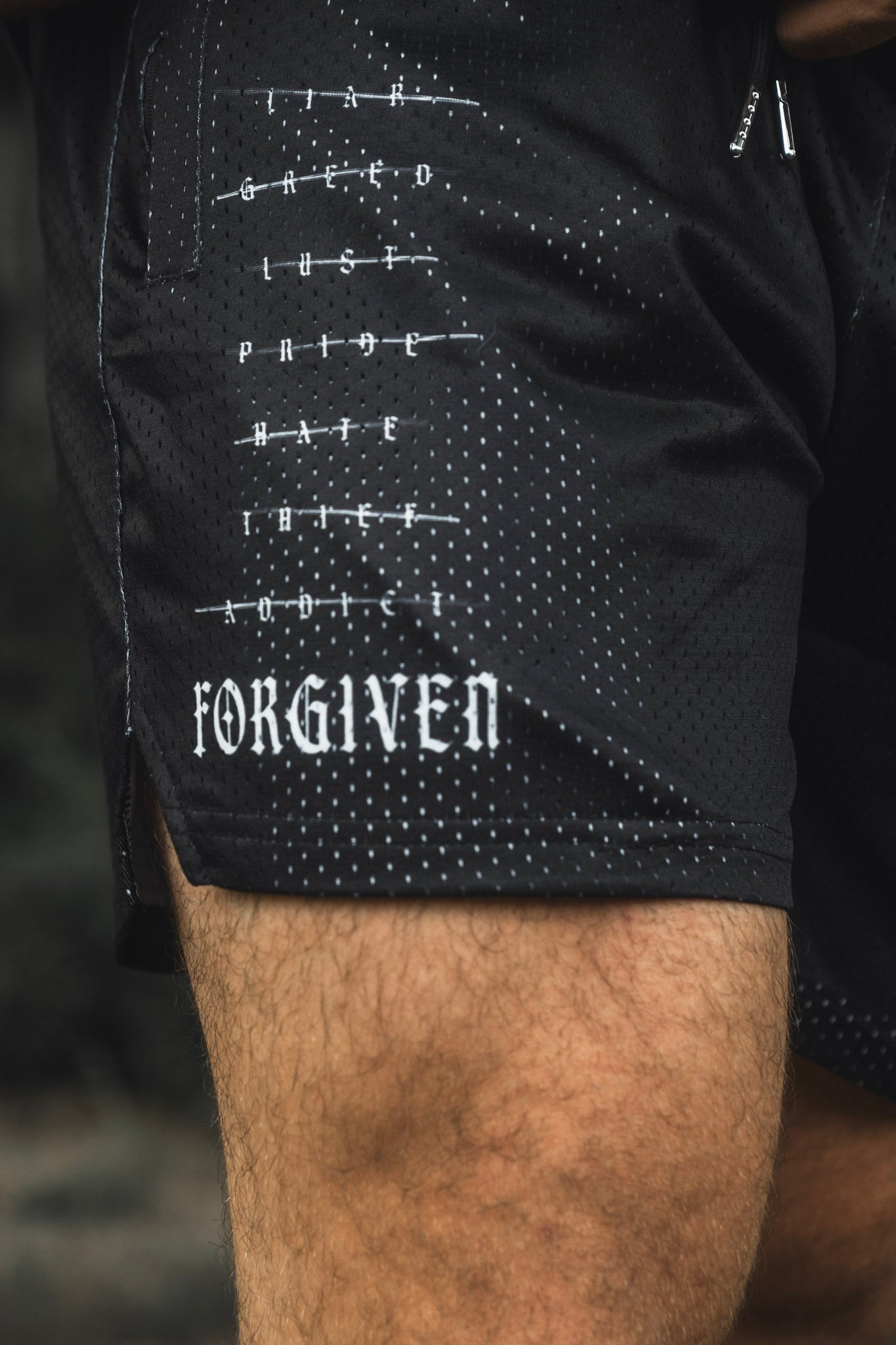 Close-up of the 13th Men’s Mesh Lifestyle Shorts | 5.5″- Forgiven, featuring words representing sins crossed out with “FORGIVEN” printed below.