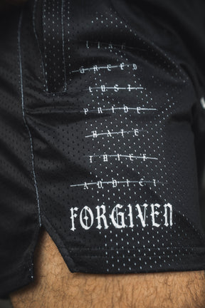 Close-up of the Men’s Mesh Lifestyle Shorts | 5.5″ - Forgiven by 13th, showcasing black mesh fabric adorned with words like greed, lust, and hate crossed out, and FORGIVEN boldly printed at the bottom in white gothic-style lettering. These unisex athletic shorts blend impactful messaging with contemporary streetwear aesthetics.
