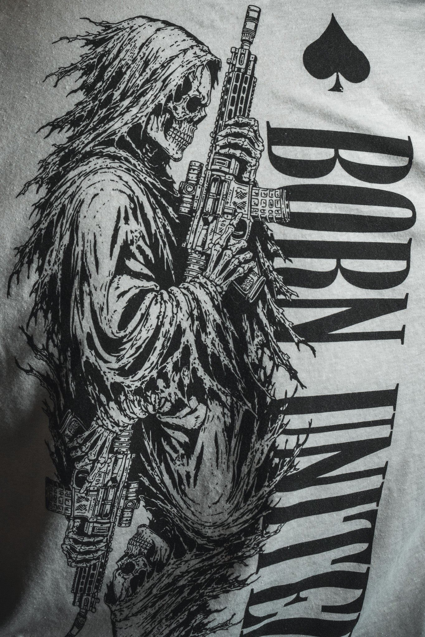 A black-and-white illustration of a grim reaper wielding a rifle, evoking dark aesthetics and wartime symbolism, is featured alongside the words “BORN UNITED” and a spade emblem—distinctly referencing the iconic Death Card tee by Born United Private Label.