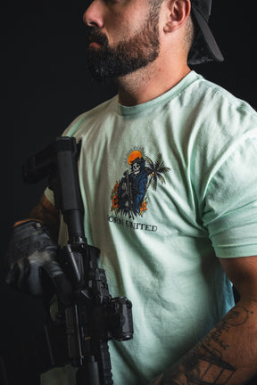 A man with a beard, wearing a backwards cap and black gloves, holds a black rifle while sporting the Born United Private Label “Always Deadly - Mint” T-shirt in an electric mint green shade with a graphic design.