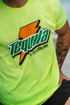 A person wearing a neon green Tango Charlie Apparel t-shirt with bold colors and a lightning bolt, featuring the text Tequila Is My Gatorade - Lemon Lime. Their tattooed arm is partially visible.