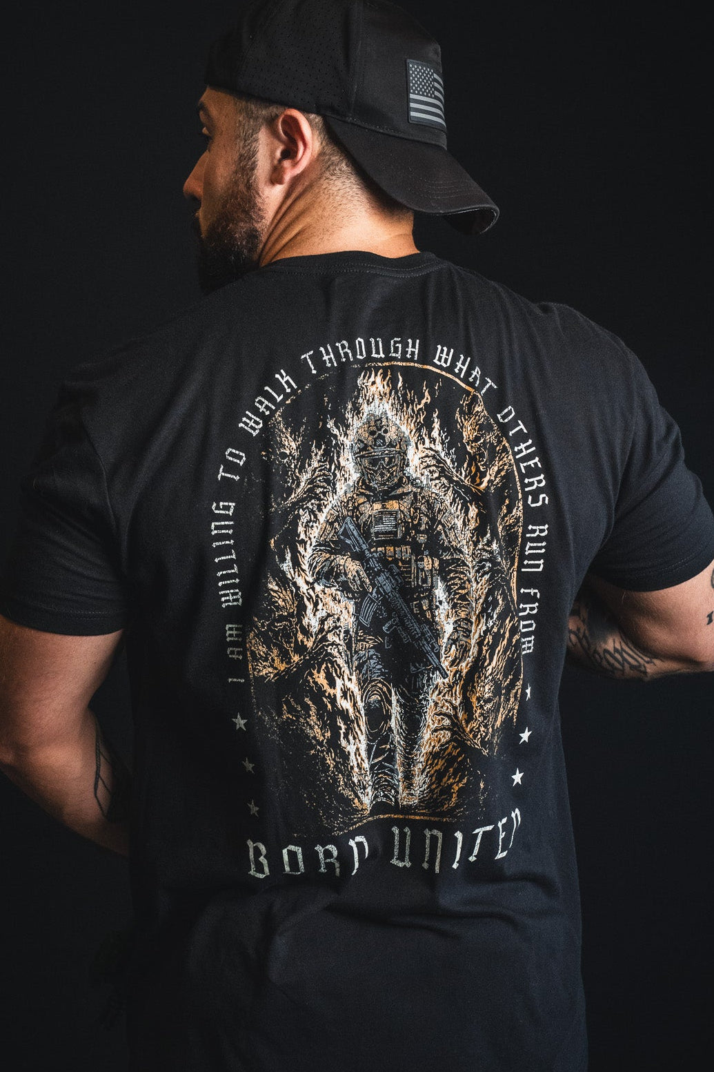 A man facing away wears the Walking Through Fire t-shirt from Born United Private Label—a premium tee featuring a soldier surrounded by flames and the empowering message, “I am willing to walk through what others run from.” This bold resilience shirt stands as a testament to strength in the face of adversity.