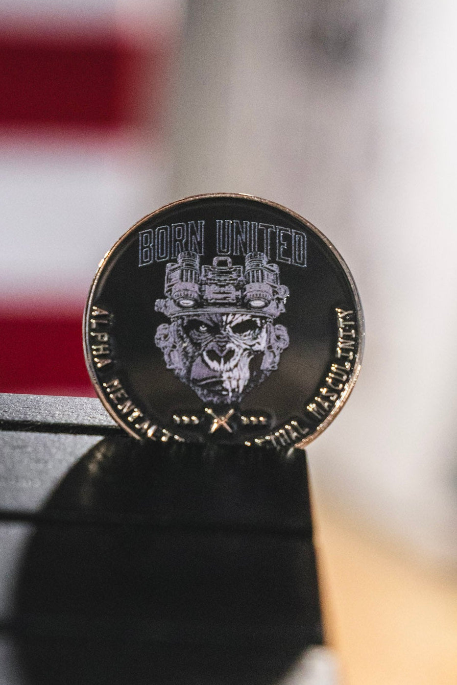 The Alpha Mentality Challenge Coin by Born United Private Label is a round metal coin showcasing a stylized gorilla head in a helmet, symbolizing an Alpha Mentality. The words “BORN UNITED” appear at the top, with additional text along the edge.