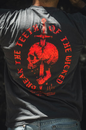 A person wearing the 13th “Break the Teeth Premium Tee,” which features a red skull pierced by a sword and the circular text “BREAK THE TEETH OF THE WICKED,” inspired by Psalm 3:7—“Deliver me, O my God.”.