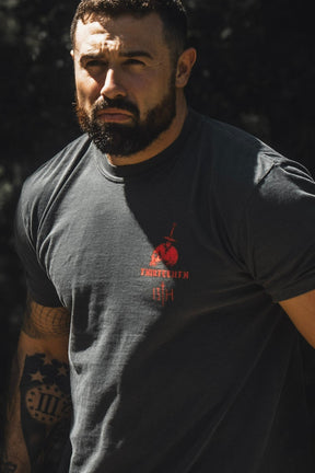 A bearded, tattooed man stands outdoors wearing the 13th “Break the Teeth Premium Tee,” a dark T-shirt with a striking red graphic and the bold text “Break the teeth of the wicked,” inspired by Psalm 3:7.