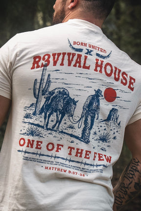 A man wearing the Revival House Premium Tee by Born United Private Label, featuring a western-inspired graphic with a red sun, cowboy, cattle, and the words “REVIVAL HOUSE ONE OF THE FEW” alongside Matthew 9:37-38—a standout piece of Christian ranch apparel that effortlessly combines rugged style with faith-driven inspiration.