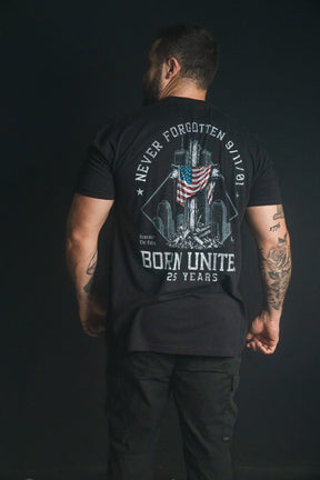 A man stands with his back to the camera, wearing a black We Remember: 25th Anniversary tee from Born United Private Label that features a September 11 memorial design and the text Never Forgotten 9/11—symbolizing honor and resilience.