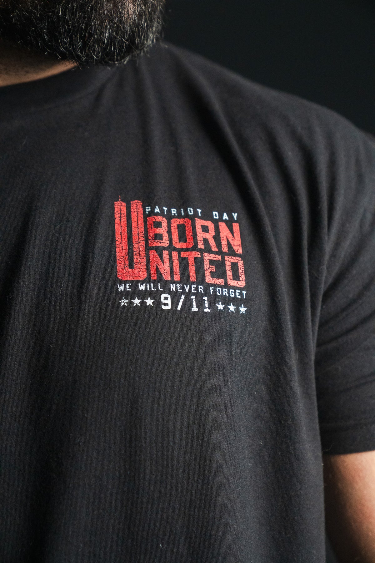 Close-up of a black “We Remember: 25th Anniversary” tee from Born United Private Label, featuring red and white text reading Patriot Day Born United, We Will Never Forget, 9/11 on the chest—a powerful emblem of honor and resilience that serves as a meaningful September 11 memorial.