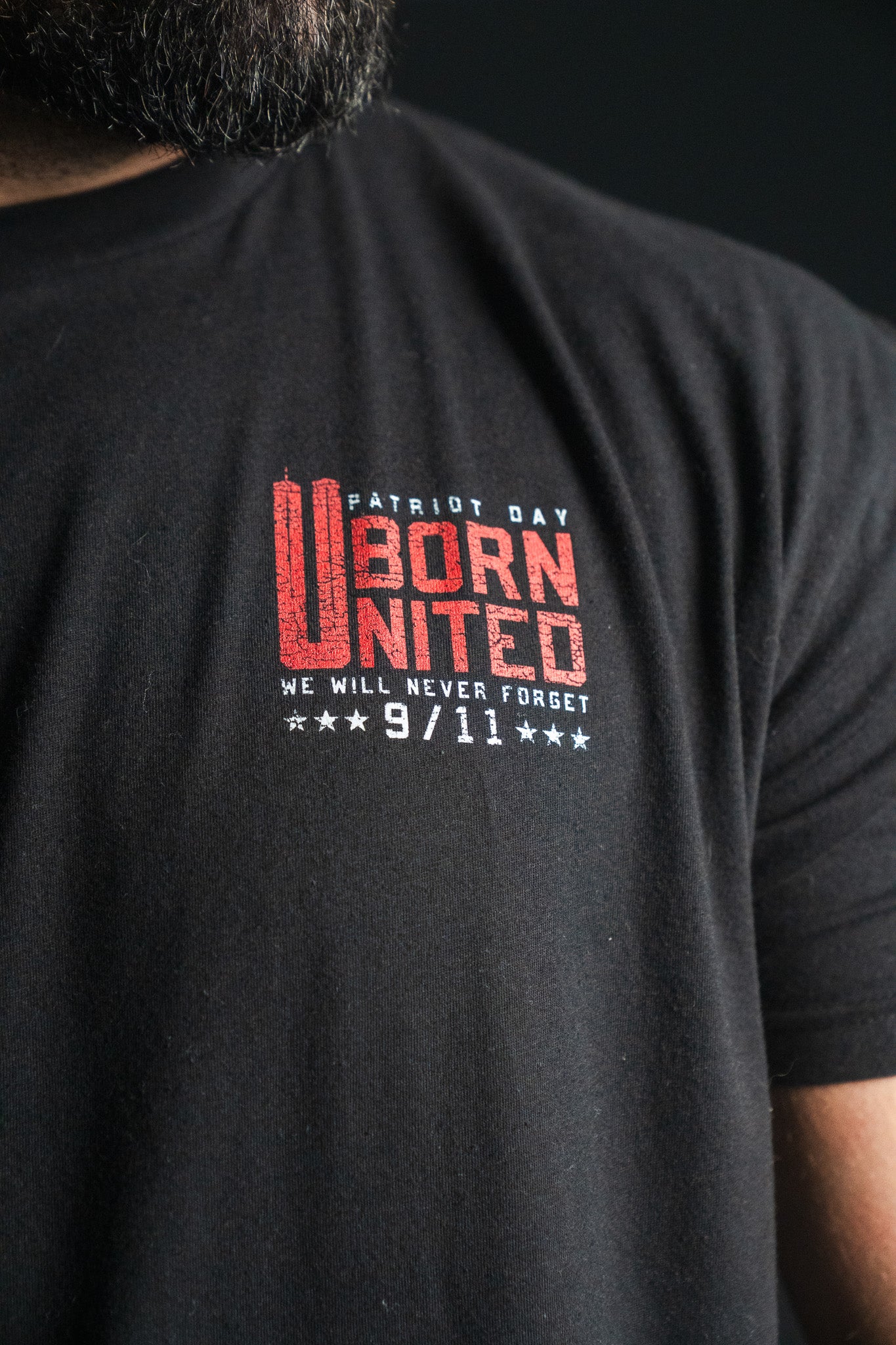 Close-up of a black “We Remember: 25th Anniversary” tee from Born United Private Label, featuring red and white text reading Patriot Day Born United, We Will Never Forget, 9/11 on the chest—a powerful emblem of honor and resilience that serves as a meaningful September 11 memorial.