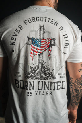 A man wearing the We Remember: 25th Anniversary - White tee from Born United Private Label, featuring a 9/11 memorial design with a cross, American flag, and the phrases “Never Forgotten 9/11/01,” “Born United 25 Years,” and “Remember the Fallen”—a tribute to honor and resilience.