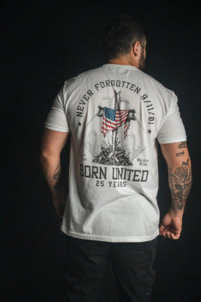 A man faces away wearing the “We Remember: 25th Anniversary - White” t-shirt by Born United Private Label, featuring an American flag, the text “Never Forgotten 9/11/01” and “Born United 25 Years,” and silhouettes of buildings—an inspiring September 11 memorial shirt honoring resilience and remembrance.