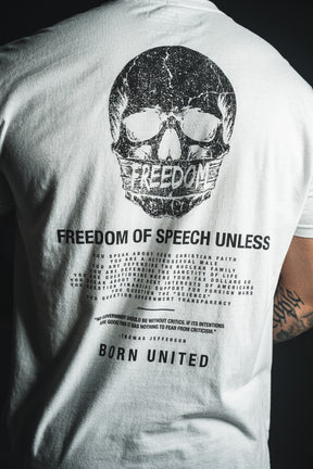 Wearing the Freedom of Speech - White t-shirt from Born United Private Label, this person sports a white tee displaying a black skull above the word “FREEDOM,” along with printed text about freedom of speech concluding in “BORN UNITED.” The design features subtle references to values such as the nuclear family and Christian faith. A tattoo is visible on their right arm.