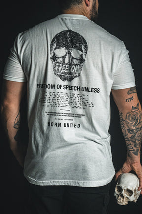 A tattooed individual holds a skull and wears the Born United Private Label’s “Freedom of Speech - White” T-shirt, featuring a large skull graphic and the words “FREEDOM OF SPEECH UNLESS” on the back, making a bold statement about freedom of speech and challenging conventional norms.