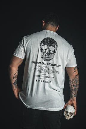 A person facing away wears the “Freedom of Speech - White” T-shirt by Born United Private Label, featuring a skull graphic and the phrase “FREEDOM OF SPEECH UNLESS”; holding a small skull in one hand, they make a subtle statement about freedom of speech.