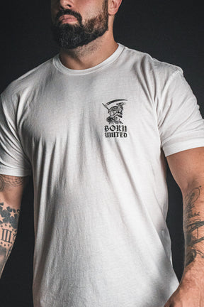 A man with tattoos wears the Born United Private Label “Memento Mori - White” t-shirt, featuring a small illustrated graphic on the upper left chest—a subtle philosophical reminder of mortality seamlessly integrated into his everyday style.
