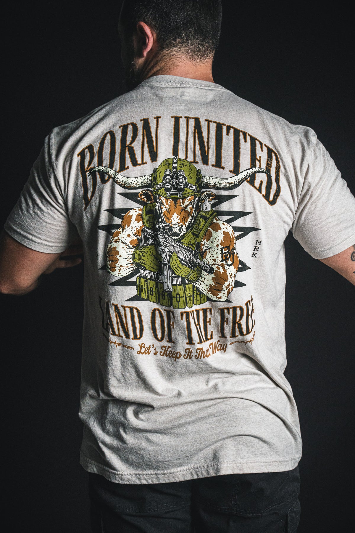A man wearing the Freedom Frontier T-shirt by Born United Private Label, featuring a bold graphic of a bull in military gear and the words “Born United, Land of the Free, Let’s Keep It That Way” on the back—a striking tribute to American values and patriotism.