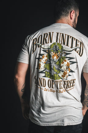 A man is shown from the back, wearing the Born United Private Label “Freedom Frontier” T-shirt—a light gray tee featuring a bold bull skull graphic with American flag motifs and the words “Born United, Land of the Free” on the back, celebrating American values and patriotism.
