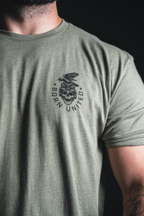 A person wearing an olive green “Only the Dead” t-shirt from Born United Private Label, featuring a skull, eagle, stars, and the words Born United on the left chest—echoing themes of remembrance and history.