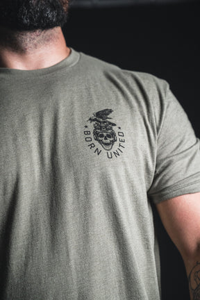 A man wearing an olive green “Only the Dead” t-shirt by Born United Private Label, featuring a striking black graphic of a skull and eagle with the words BORN UNITED across the chest—a bold design inspired by classic wartime spirit.