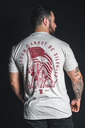 A man wearing the Born United Private Label “Freedom Not Silenced” light gray T-shirt, which showcases an illustration of a Revolutionary War soldier proudly holding an American flag and features the impactful message “Freedom cannot be silenced, Born United” on the back.