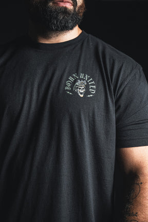 A man with a beard wearing a black t-shirt from Born United Private Label, featuring a small skull graphic and the “Compliant We Fall” text on the upper left chest, paired with the bold phrase “Defiant we Stand” for an added touch of inspiration.