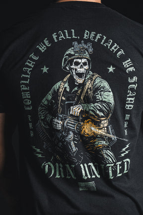 A person wears the Born United Private Label “Compliant We Fall” black shirt, which features an illustration of a skeleton soldier firing a weapon along with the bold phrases “Compliant We Fall, Defiant We Stand” and “Odin United.”.