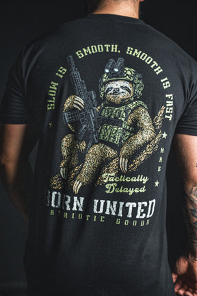 A black Tactically Delayed Tee featuring a sloth in tactical gear holding a rifle, with text reading Slow is smooth, smooth is fast, and Born United Patriotic Goods.
