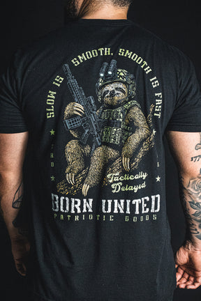 A person wears a Tactically Delayed Tee featuring a sloth in tactical gear holding a rifle, surrounded by the text Slow is smooth, smooth is fast and Tactically Delayed.