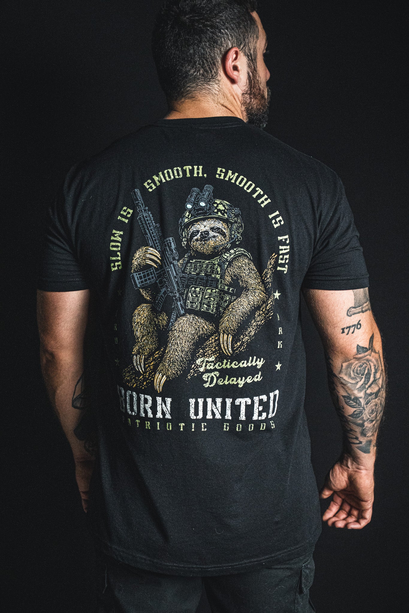 Back view of a person wearing a black Born United Private Label Tactically Delayed Tee featuring a sloth in military gear holding a rifle with the text Slow is smooth, smooth is fast.