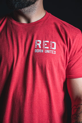 A person wearing a Born United Private Label RFV2 red T-shirt, featuring the text RED BORN UNITED printed on the upper chest. Only the torso, right arm, and part of the face are visible, with the shirt’s vibrant color subtly conveying a Remember Everyone Deployed message.