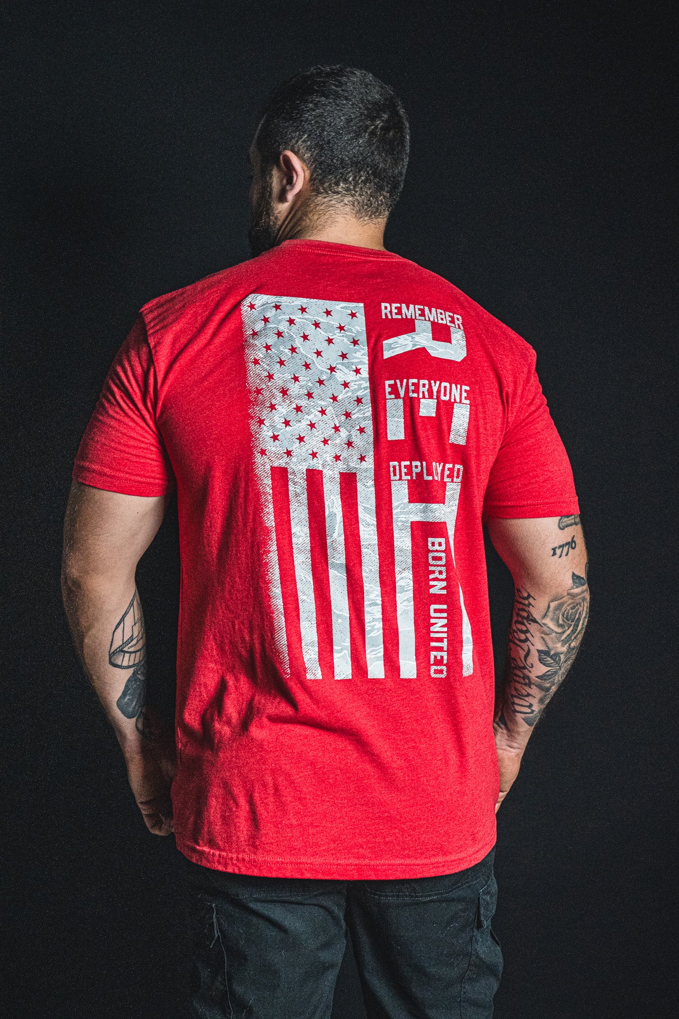 A man is facing away, wearing the Born United Private Label RFV2 red t-shirt featuring an American flag and the words “Remember Everyone Deployed V2” and “Born United” printed on the back.