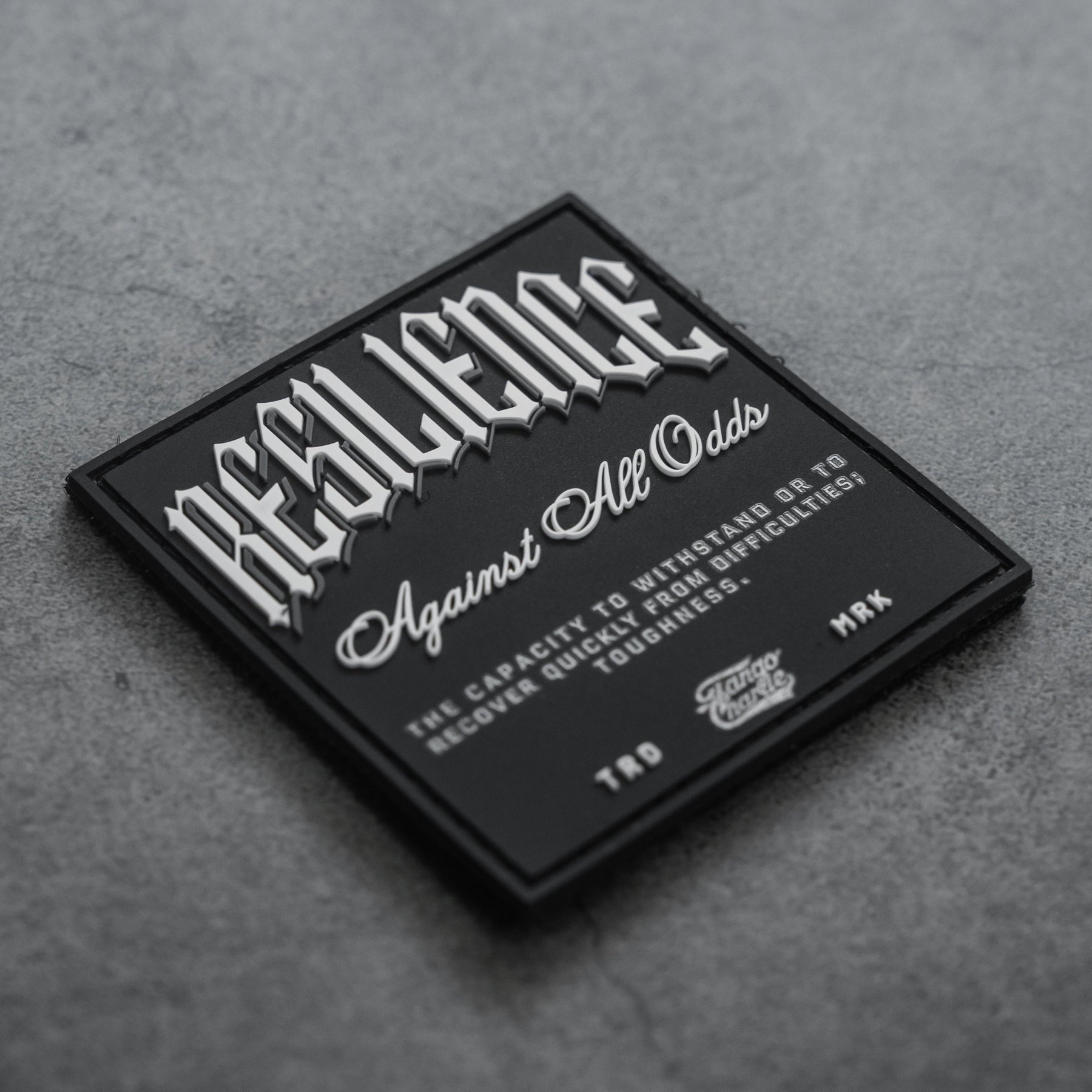The Resilience - Patch by Tango Charlie Apparel features a black 3D PVC design with “RESILIENCE” in bold white on grey, “Against All Odds” below, plus text defining resilience. Credits note TTD, MRK, and Savage Supply Co. It’s a 3-inch Velcro patch.