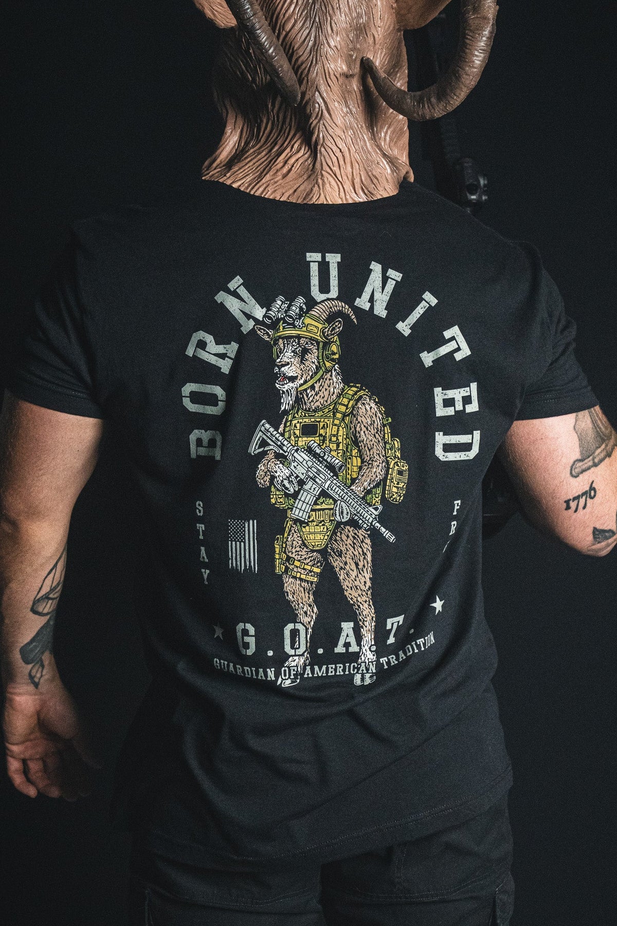 A person wearing the Born United Private Label “G.O.A.T.” shirt, which features an armed goat in tactical gear alongside the phrases “Born United” and “G.O.A.T. Guardian of American Tradition,” making this statement tee a bold celebration of American tradition.
